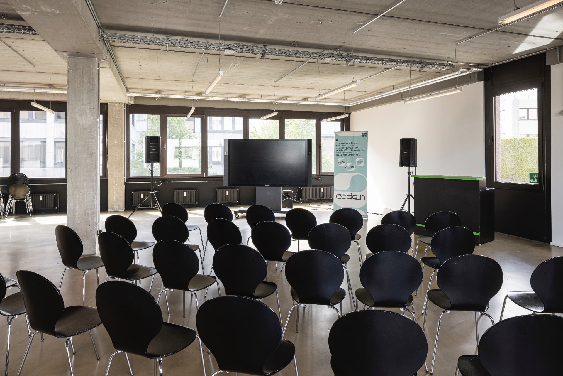 Event Area mit Stuhlreihen, großem Bildschirm, Lautsprechern und Bartresen