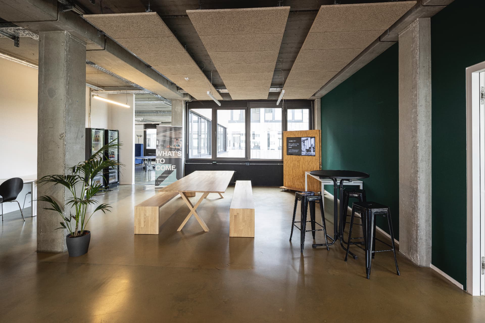 Community lounge with long wooden bench-table under acoustic ceiling panels