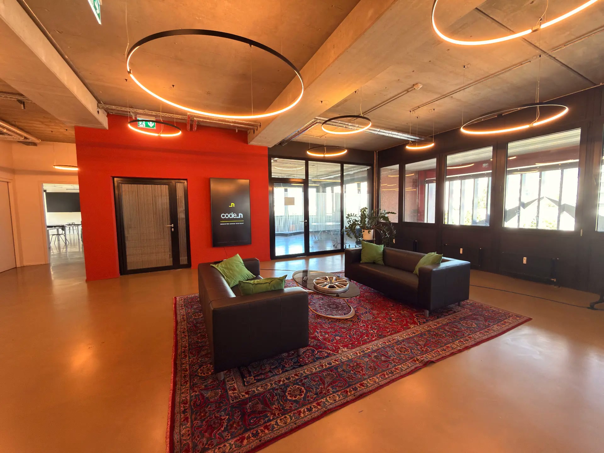 code_n reception lounge with black leather sofas, green cushions, circular ceiling lights and a red feature wall with the code_n logo