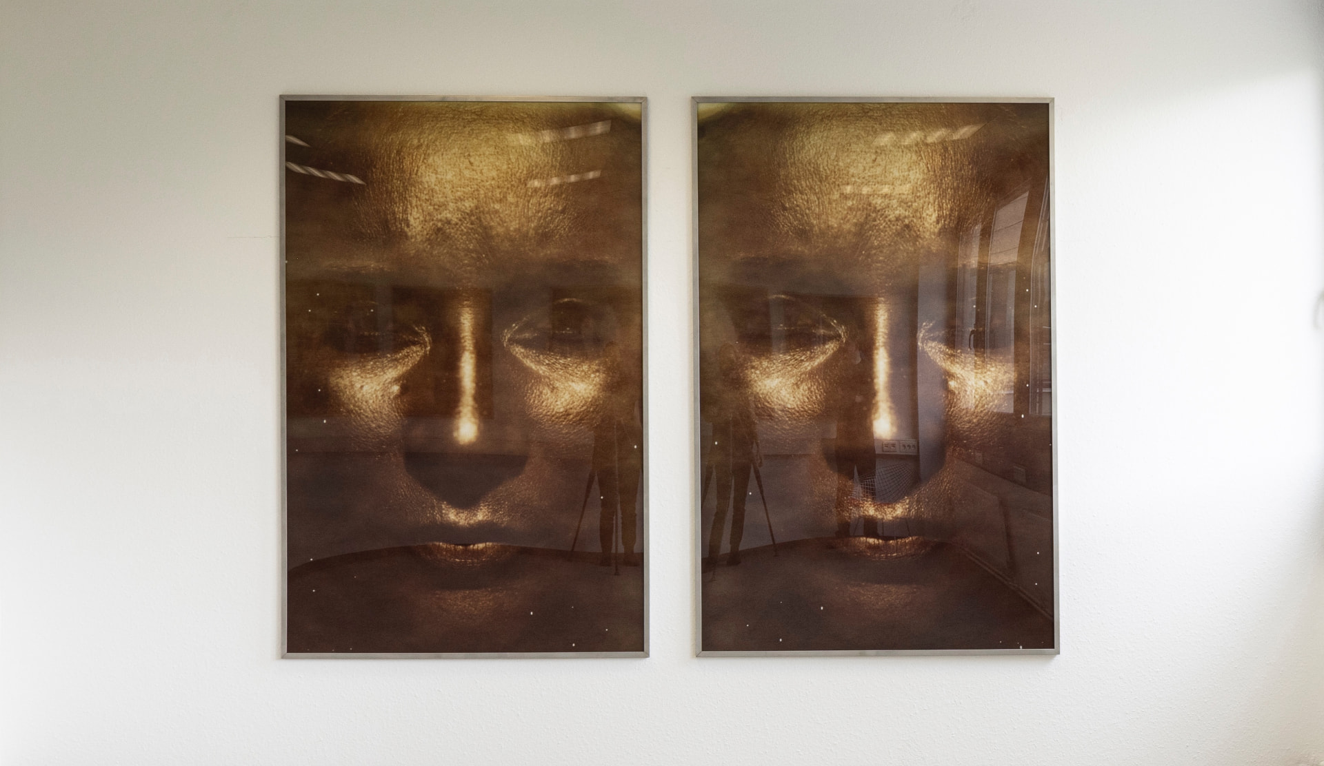 Golden-toned photographic diptych of a face, hung on a white wall