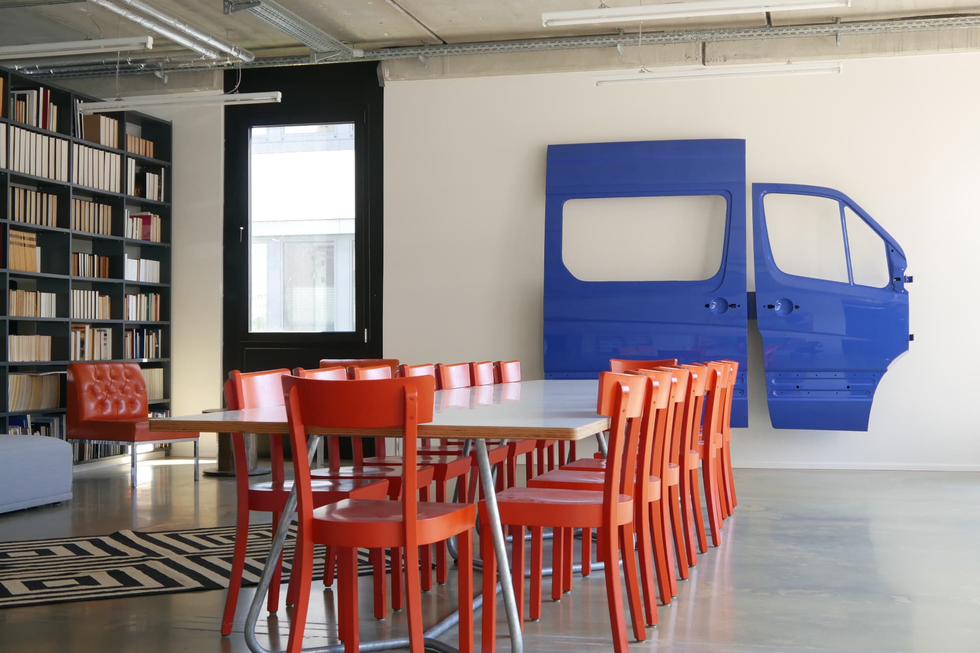 Library room with wooden bookshelves, red chairs and a blue van-door installation
